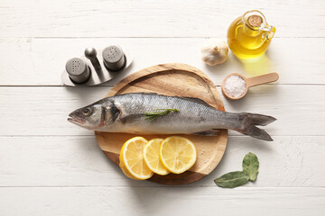 Plate with fresh raw seabass fish and different spices on white wooden background