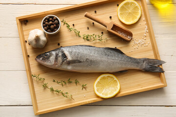 Tray with fresh raw seabass fish and different spices on white wooden background