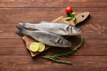Cutting board with fresh raw seabass fishes and different ingredients on wooden background