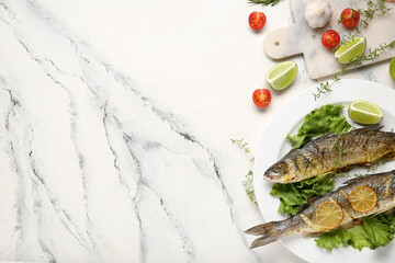 Plate with delicious cooked seabass fish, lettuce, herbs, tomatoes and lime slices on marble background