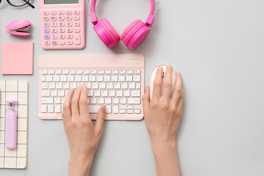 Female hands with modern computer keyboard, mouse, headphones and stationery on grey background