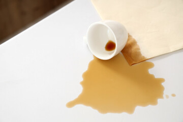 Overturned cup with spilled coffee and paper napkin on counter in kitchen, closeup