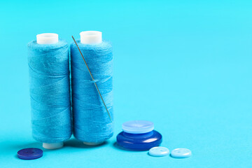 Spools of thread with needle and buttons on blue background