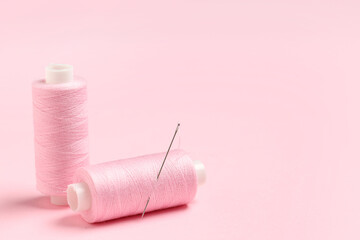 Spools of thread with needle on pink background