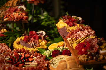 Table decorated with fruits and flowers, where there are hams, cheeses and assorted nuts in an elegant party