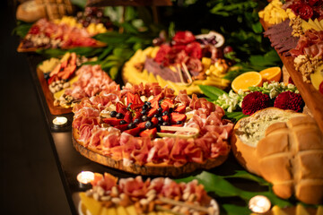 Table decorated with fruits and flowers, where there are hams, cheeses and assorted nuts in an elegant party