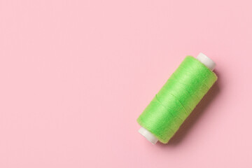 Green sewing thread spool on pink background, closeup