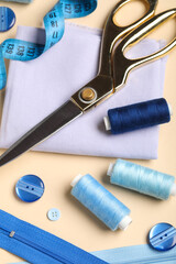 Composition with thread spools, fabric, buttons and scissors on beige background, closeup