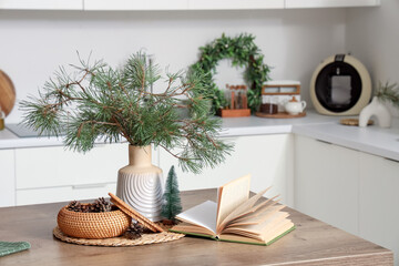 Coniferous cones with pine tree branches and book on table in kitchen