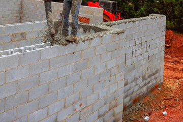 Construction worker pours cement on wall being built, surrounded by dirt machinery in work daytime