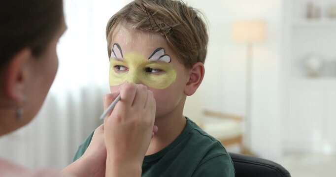 Woman drawing bee on boy's face indoors, closeup