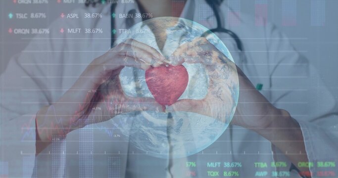 Holding red heart model, doctor in lab coat with stethoscope showing globe finance charts in clinic