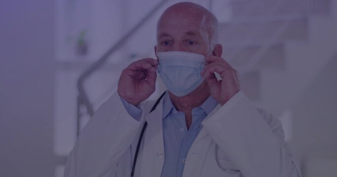 Positioning senior male doctor adjusting surgical mask in bright medical corridor, with stethoscope