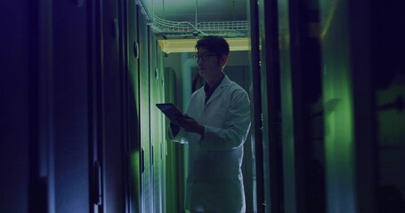 Technician wearing white lab coat inspecting server racks and trays in server room using tablet