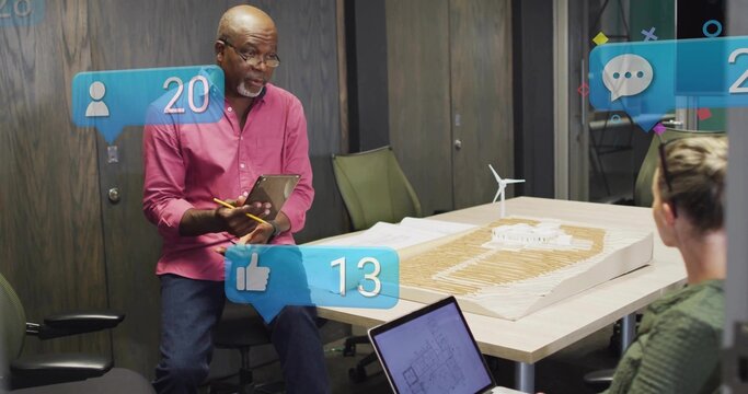 Presenting architect wearing pink shirt and jeans at conference table, with scale model, tablet - Powered by Adobe