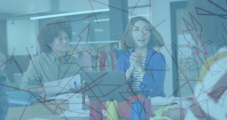 Reviewing sketches four designers collaborating around desk in studio, with glass board and laptop