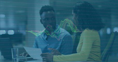 Reviewing woman holding printed document with man typing laptop at office desk, line graph overlay