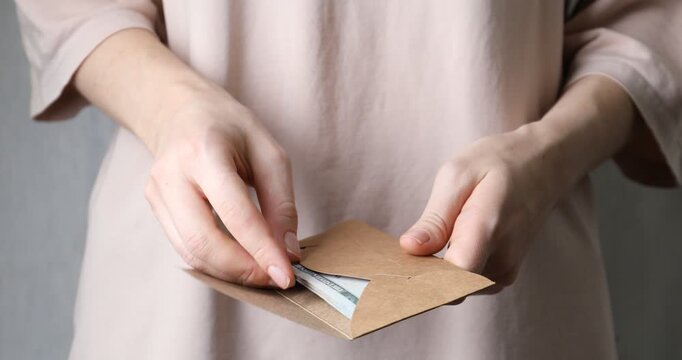 Alimony. Woman putting money into envelope on blurred background, closeup