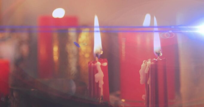 On blue lens flare entering frame, two slender red candles burning and dripping, creating warm glow