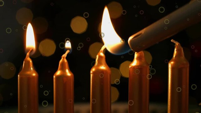 Entering lighter nozzle, igniting five gold taper candles one by one creating festive glow