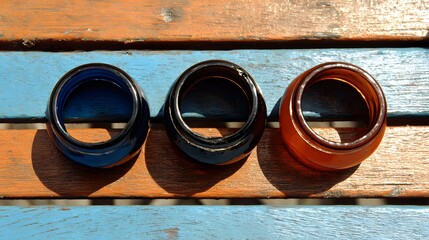 Three colorful glass bangles rest on a weathered wooden surface.