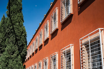 Naklejka premium Red building facade with white metal window bars and blue sky