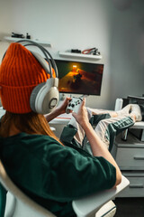 Young woman wearing orange hat and headset playing console game at home, smiling and enjoying leisure. Concept of cozy lifestyle, gaming fun and modern entertainment. © Aboltin