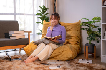 Young woman yawning while reading a book in cozy living room