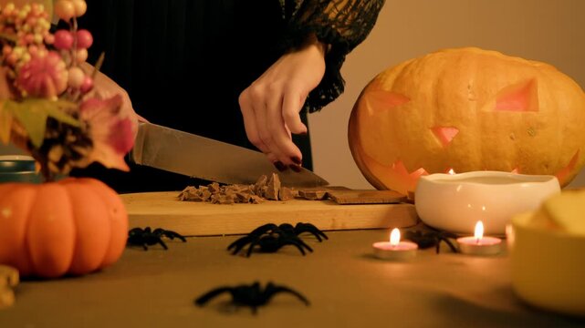 Sharp knife crushes chocolate bar into chunks on a board, table is decorated for a holiday with Halloween spiders