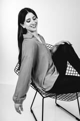 Fashion black and white portrait of a beautiful brunette woman smiling in a styling outfit on light gray studio background