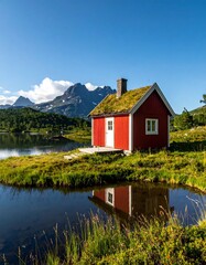 Obraz premium A vibrant red cabin with a green rooftop sits beside a calm lake with mountains in the distance under a clear blue sky