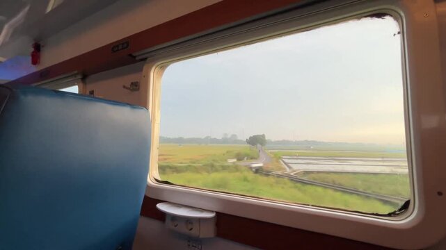 View from the train window. Beautiful view from the window of a long-distance train, with green rice fields stretching out and residential areas on the edge of the rice fields during a light rain.