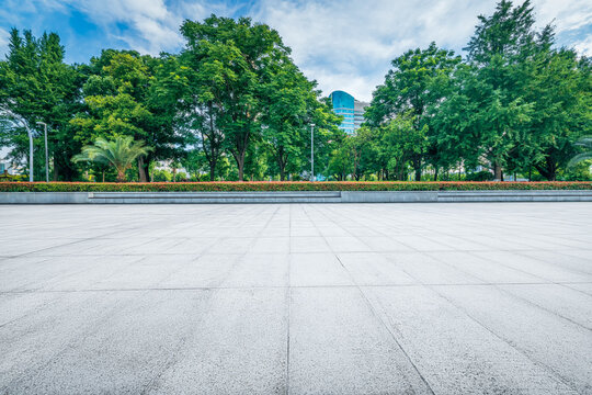 Empty square stone floor in public park on a sunny day with lush green trees in the background.