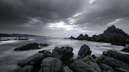 Dramatic black and white seascape with rocky shore and cloudy sky at sunset