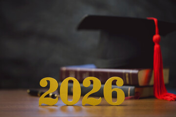 Golden 2026 numbers with graduation cap and stacked textbooks on a wooden desk, symbolizing Class of 2026, academic achievement, commencement celebration, education goals, future planning, and success