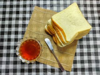 Golden liquid honey in a delicate glass bowl, perfectly paired with a stack of soft white bread slices and a spreader, ready for a wholesome and sweet breakfast