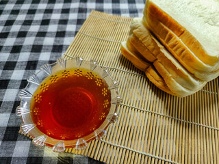A close-up view of delicious honey in a glass bowl next to freshly sliced white bread on a bamboo mat