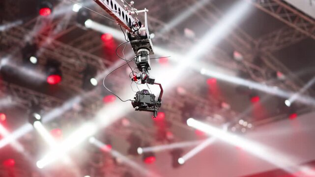 Camera crane captures an aerial view of a lively concert under bright colored and flashing lights