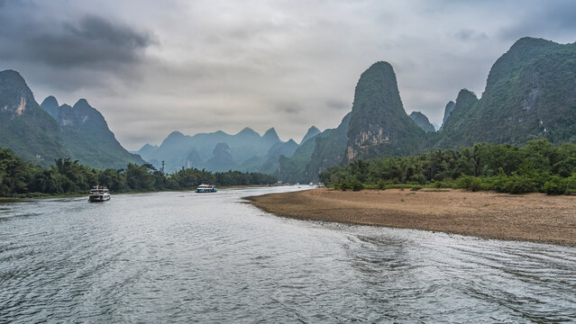 Tourist ships sail along the picturesque river. The riverbed bends. Green vegetation on the shores. Beautiful mountains against the sky and clouds. China. Li River. Li Jiang. Guilin