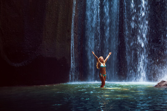 Woman stand in underground cave pool under falling fresh water of Tukad Cepung waterfall. Nature day tour, hiking activity adventure and fun at family tourist camp on summer vacation in Bali island - Powered by Adobe