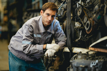 White man technician checking used car damaged engine block at scrap yard warehouse recycle area...