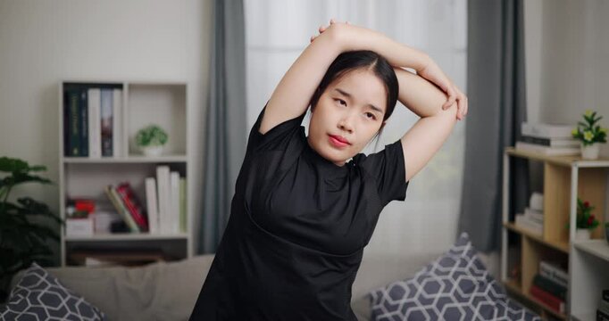 Handheld front view shot, Relaxed Asian woman is exercising by stretching in the living room at home. Healthy Lifestyle Concepts. Women Lifestyle