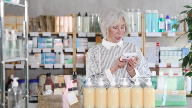 Mature woman stands in front of the shelves in the pharmacy and chooses paracetamol from different manufacturers. Pensioner in a European pharmacy does shopping