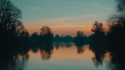 Fototapeta premium Serene lake with orange sky during sunrise or sunset, reflective water surface mirrors trees along banks,