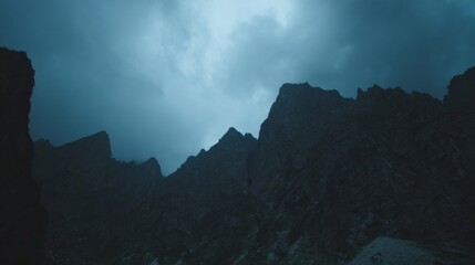 Rugged mountain landscape under a deep blue sky with grayish white clouds, towering peaks with uneven rocky surfaces,