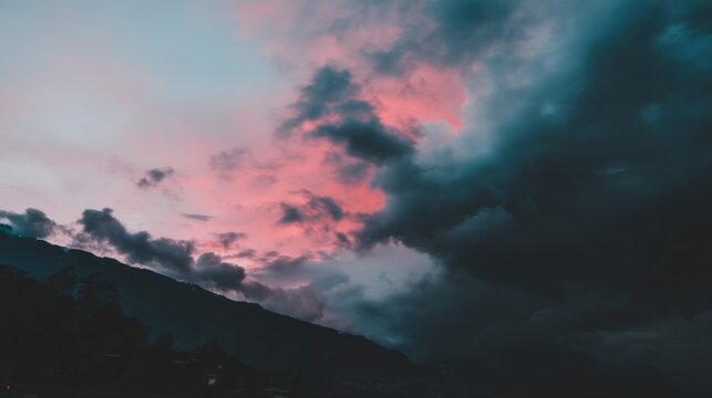 Dramatic sunrise or sunset landscape with pink purple blue sky reflecting on dense clouds rolling hills silhouette moody