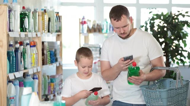 Dad teaches his son to scan QR code on package of dishwashing. Store visitors study product information in mobile app before purchasing, using QR code and smartphone camera