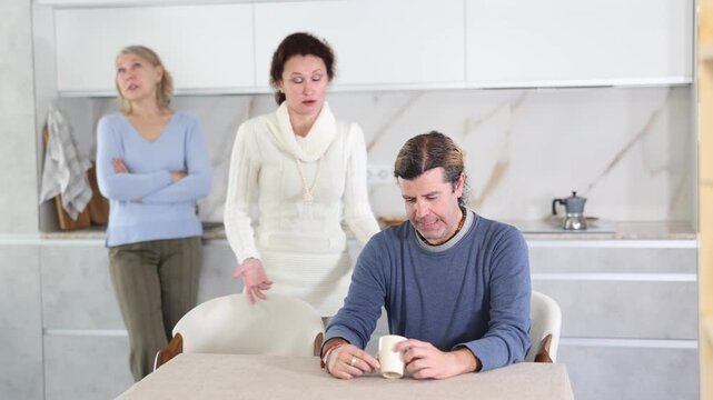 Elderly mother and woman scold swear at man. Male is upset because of family conflict, dejectedly listens to his wife and mother scolding him. Complex intergenerational relationships 