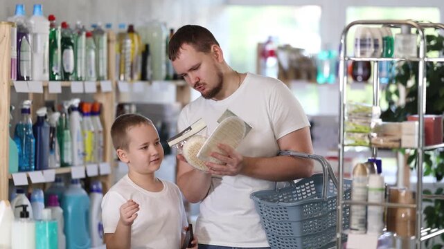 Dad tells son about choosing household goods, shows him suitable bast wisp, and explains what to look for quality when buying. Family shopping in household department
