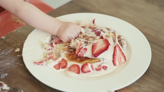 One-year-old celebrating first birthday with strawberry pancake smash cake